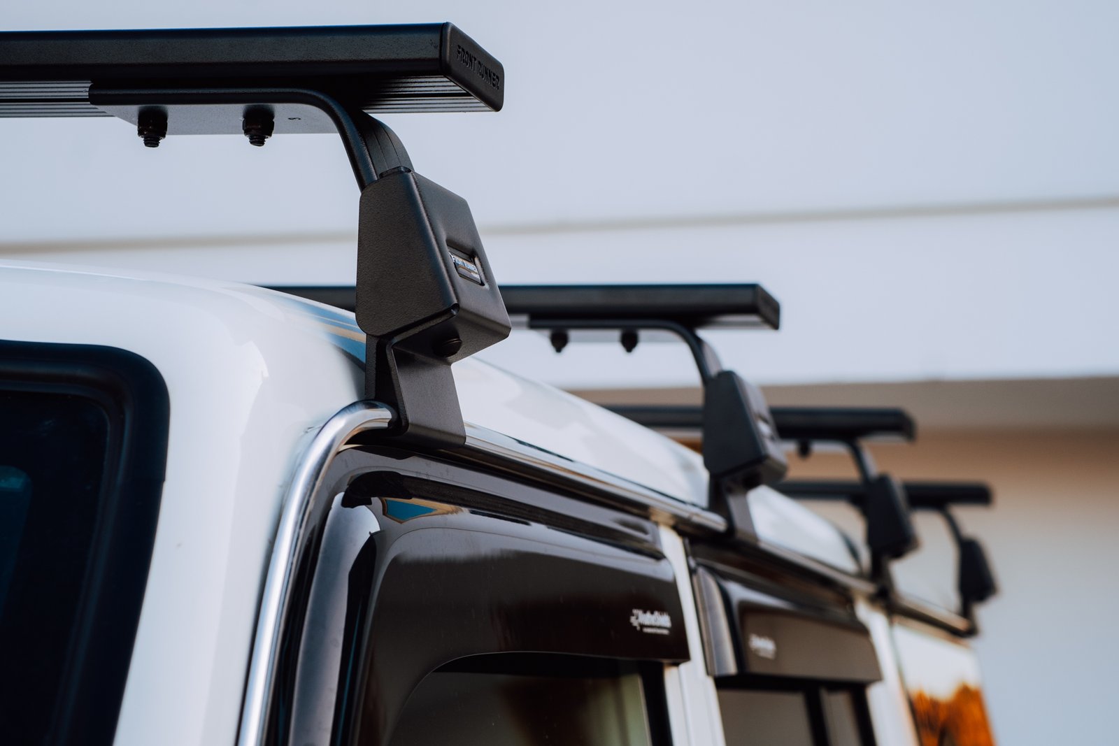 Close-up of Front Runner load bars on gutter mounts along the roof of a white Land Cruiser 76